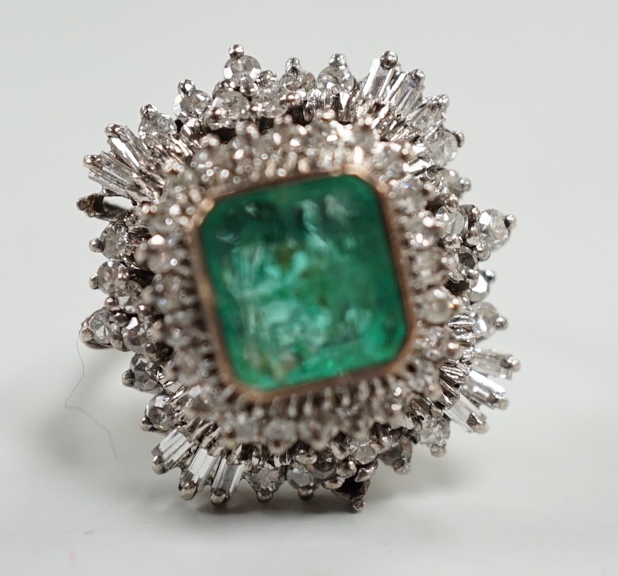 A white metal and single stone emerald set dress ring, bordered with two stepped bands of round and baguette cut diamonds, size K, gross weight 7.6 grams.
